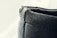 A close-up view of a textured, dark-colored leather edge with visible stitching. The surface appears slightly worn and rugged, with some frayed edges on the top side.