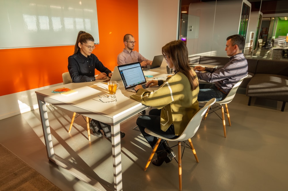 a group of people sitting around a table with laptops