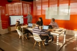a group of people sitting around a table with laptops