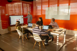 a group of people sitting around a table with laptops