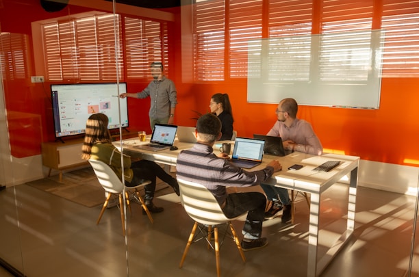 a group of people sitting around a table with laptops