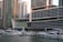 A marina filled with numerous white yachts and boats docked on calm water in front of modern high-rise buildings. The buildings feature a sleek, contemporary design with large glass windows and multiple balconies. The area appears to be a bustling urban setting with a focus on luxury and waterfront living.