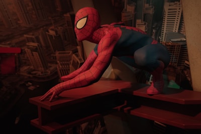 A silhouette of Spider-Man swinging through the city streets with streaks of red and blue light trailing behind.