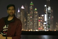A happy man holding a lottery ticket with a city skyline in the background.