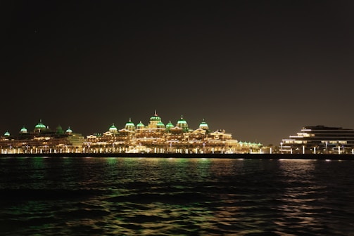 A nighttime view of the resort’s illuminated facade reflecting over calm water.