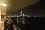 Couple smiling aboard a marina cruise with city lights reflecting on water.