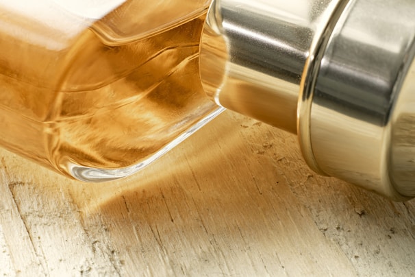Close-up of a glass bottle filled with golden argan oil, resting on a light oak surface with soft natural light.