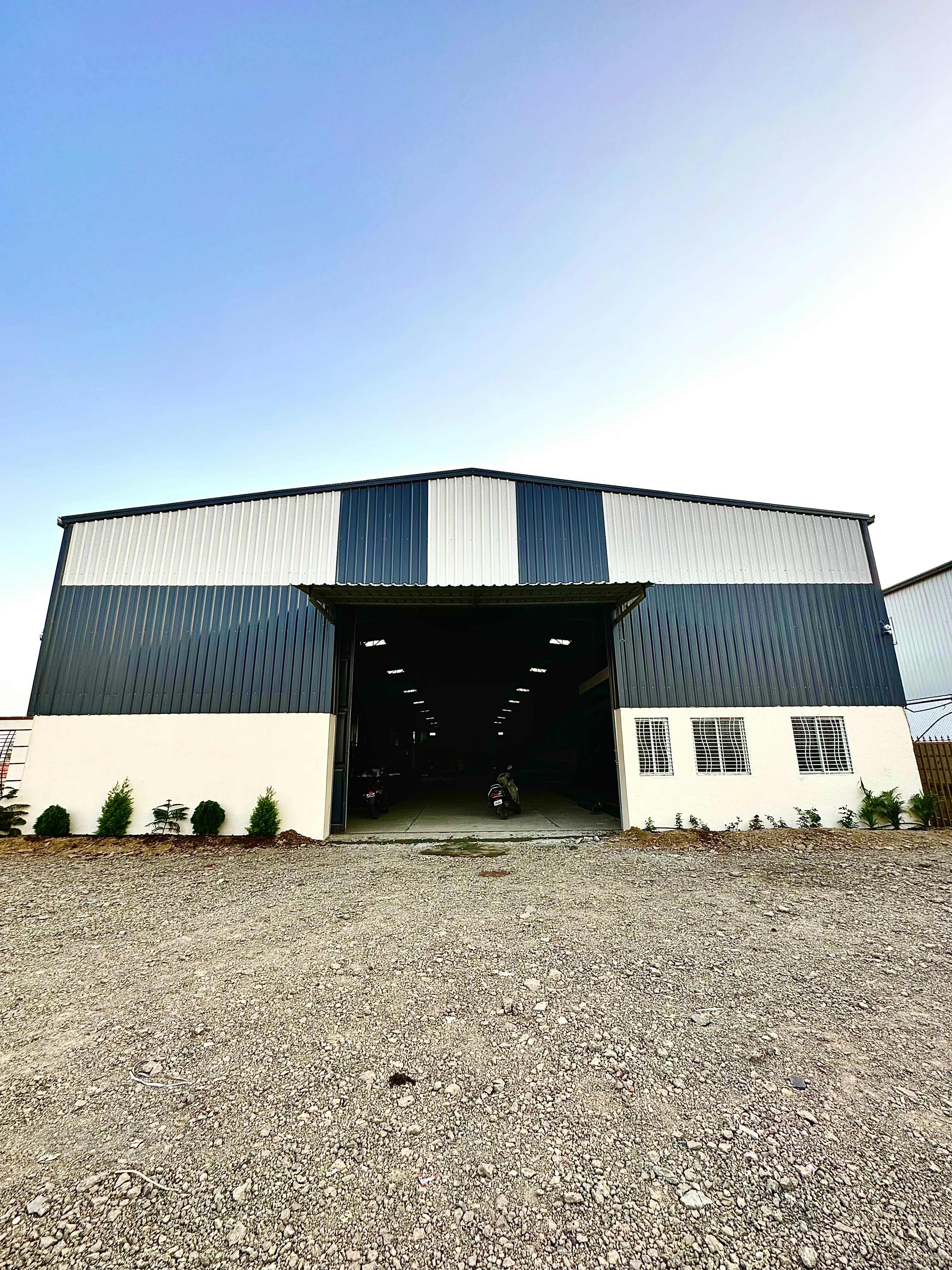 Large industrial warehouse exterior in daylight, corrugated steel walls, clear blue sky background, well-lit environment