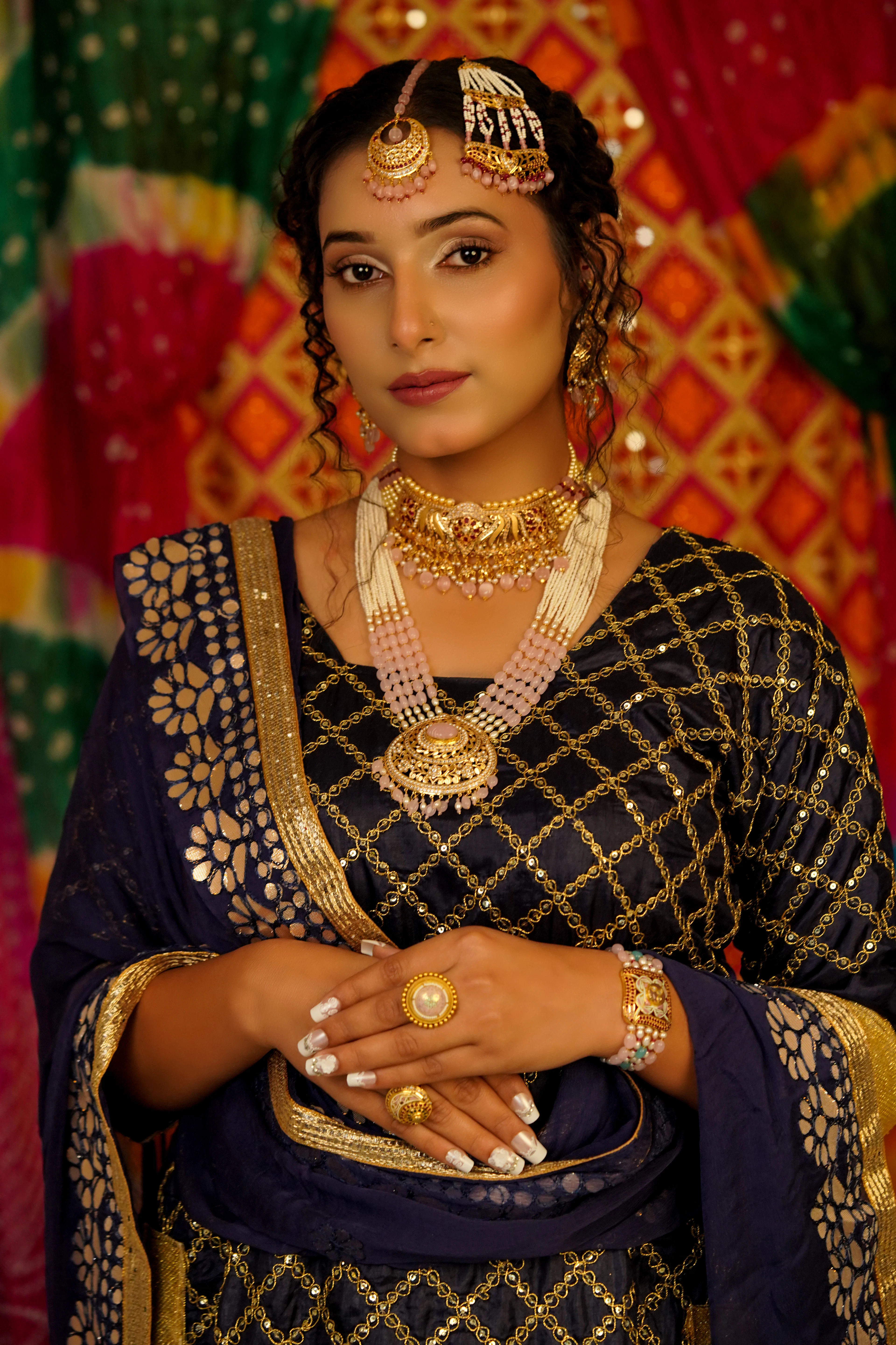 A woman in a navy dupatta wearing a gold choker, layered pearl strands and a maang tikka