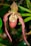 An exotic, pendulous orchid with elongated, slender petals that curve gracefully downward. The flower features a mix of deep red and peachy hues with a speckled pattern on the lip. It is set against a lush, green, blurred background that enhances its intricate details.
