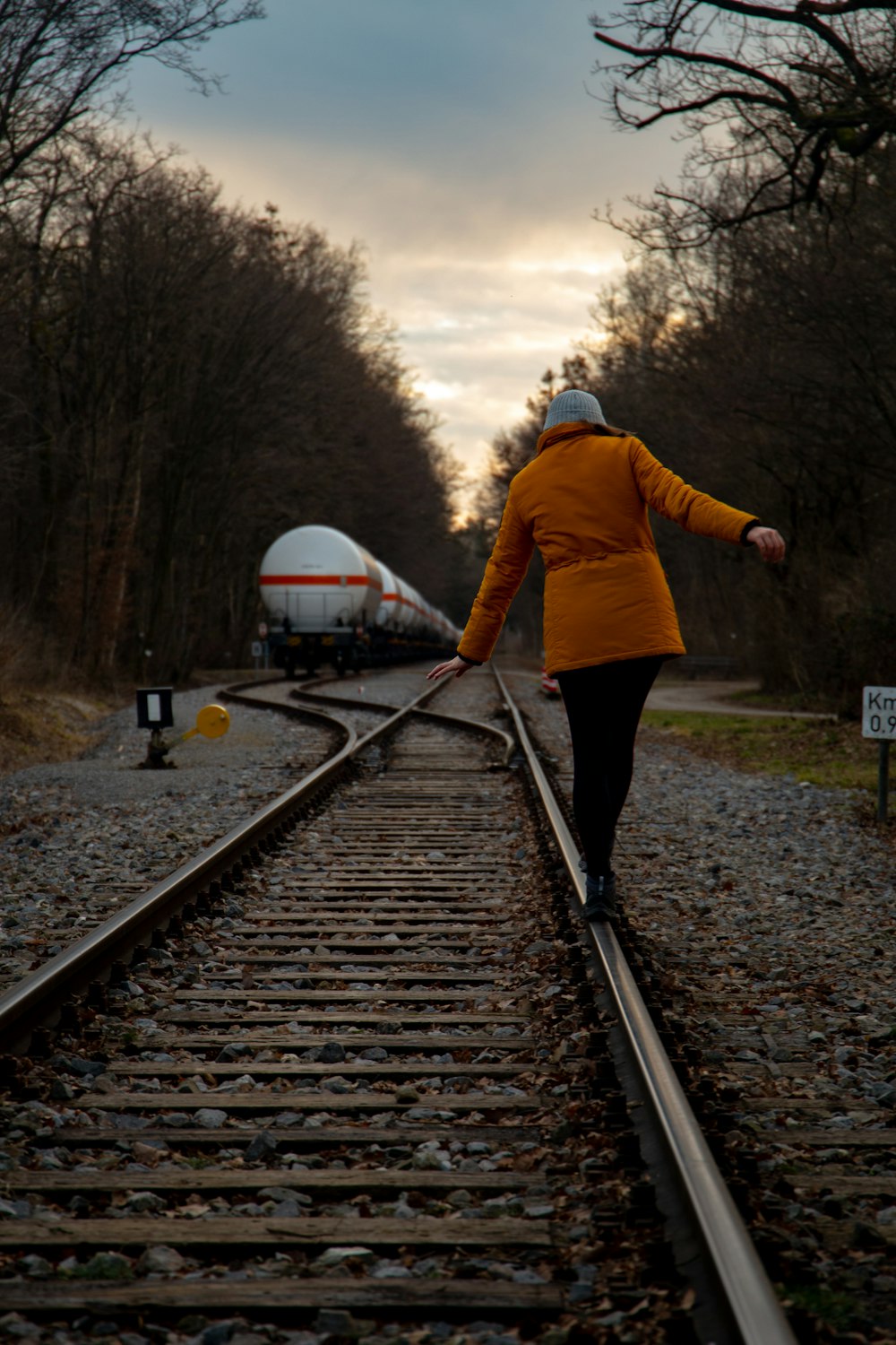 노란 재킷을 입은 여자가 기차 선로를 걷고 있다