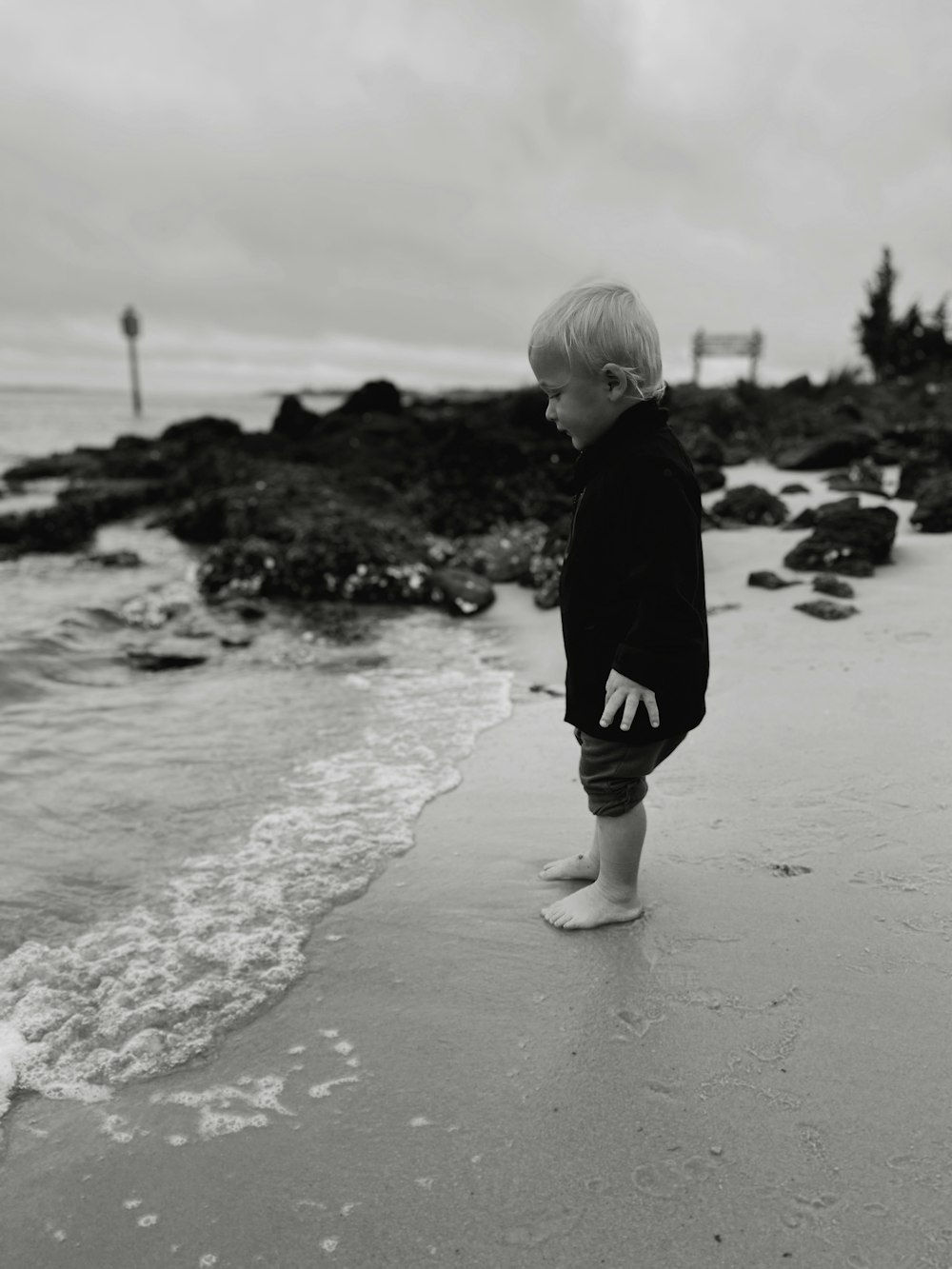 a little boy standing on top of a beach next to the ocean