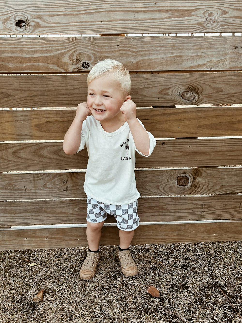 a little boy standing in front of a wooden fence