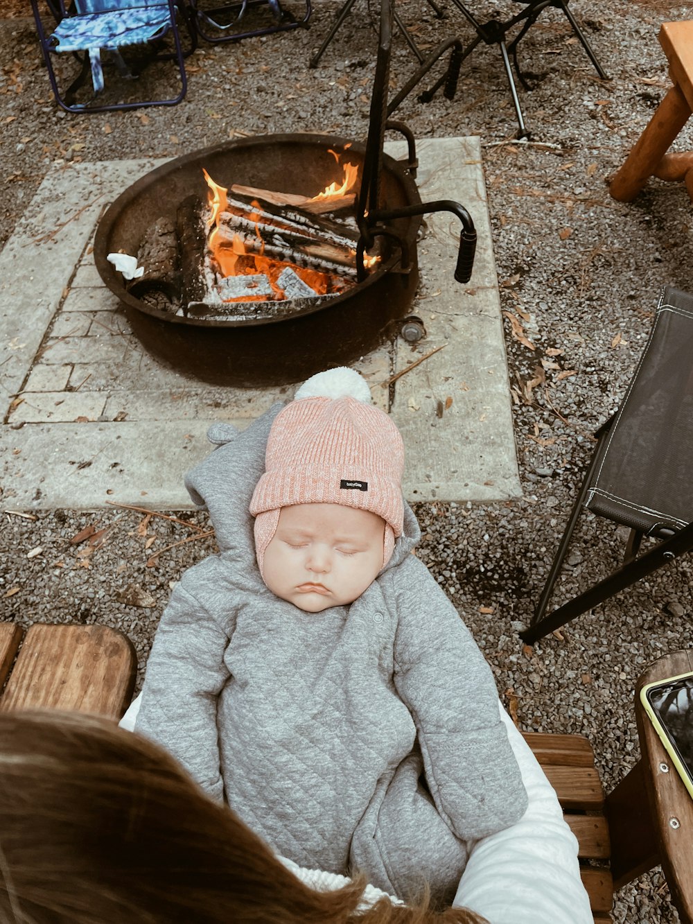 a baby wearing a pink hat sitting in front of a fire pit