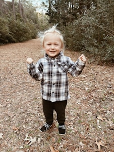 A cheerful child with a backpack exploring a sunny camp site in Vancouver surrounded by tall pine trees.