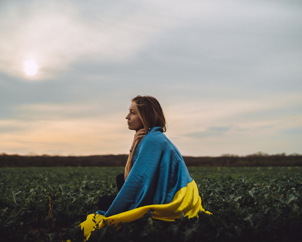 a woman sitting in a field with a blue and yellow blanket