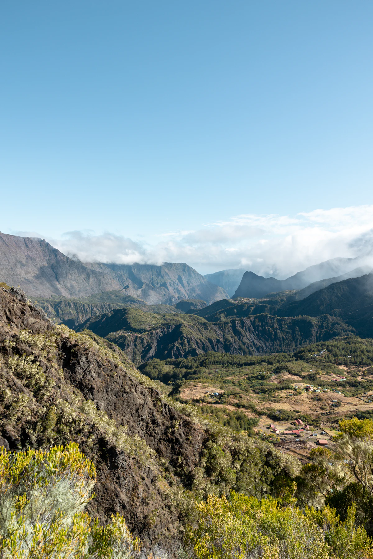 A dry ridge above a valley in the Cirque de Mafate, with a hamlet on the flat ground and peaks behind