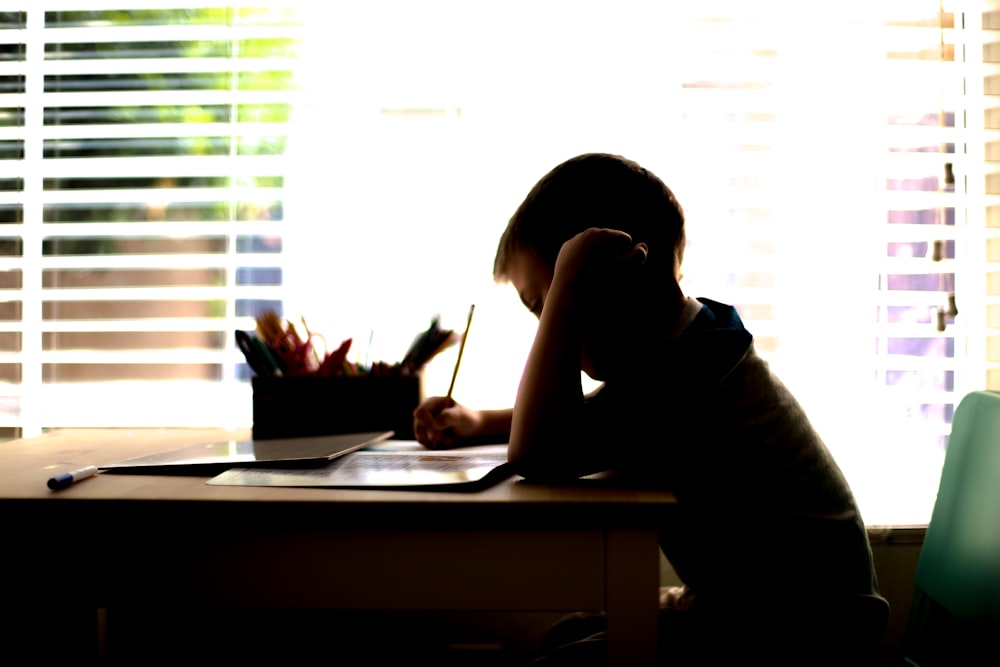 a little boy sitting at a desk writing on a piece of paper