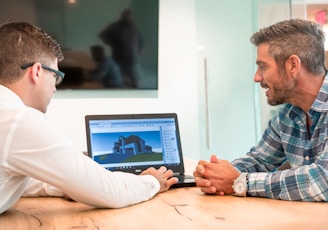 two men sitting at a table with a laptop