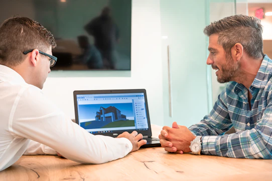 two men sitting at a table with a laptop