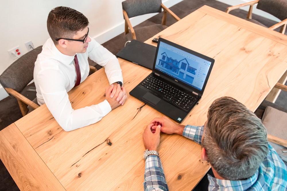 two men sitting at a table with a laptop