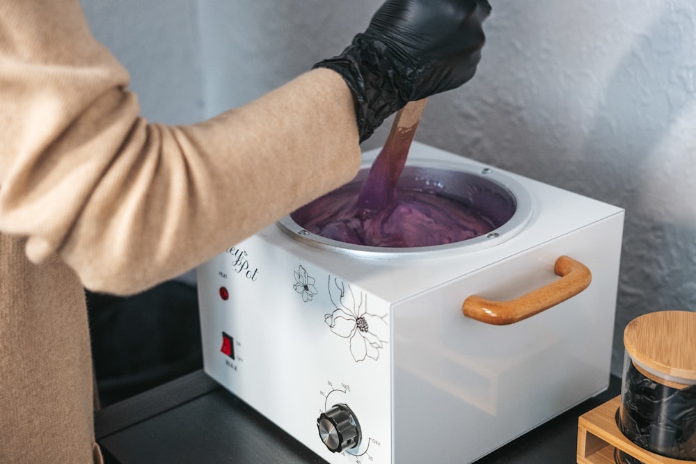 a person in black gloves stirring a pot of purple liquid