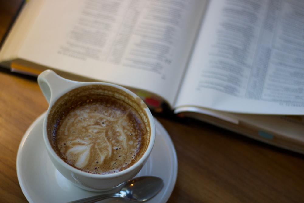 a cup of cappuccino on a saucer next to an open book