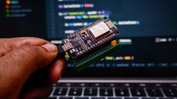 a person holding a small device in front of a laptop