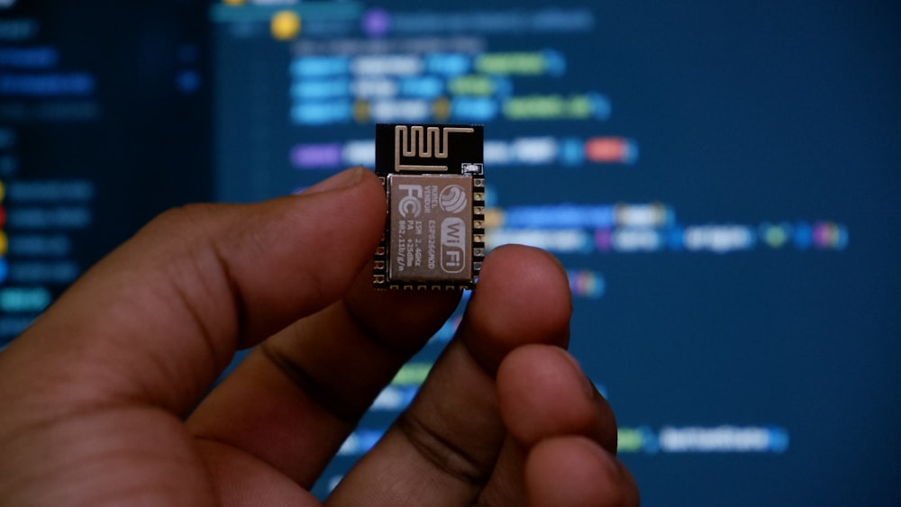 a hand holding a micro processor chip in front of a computer screen