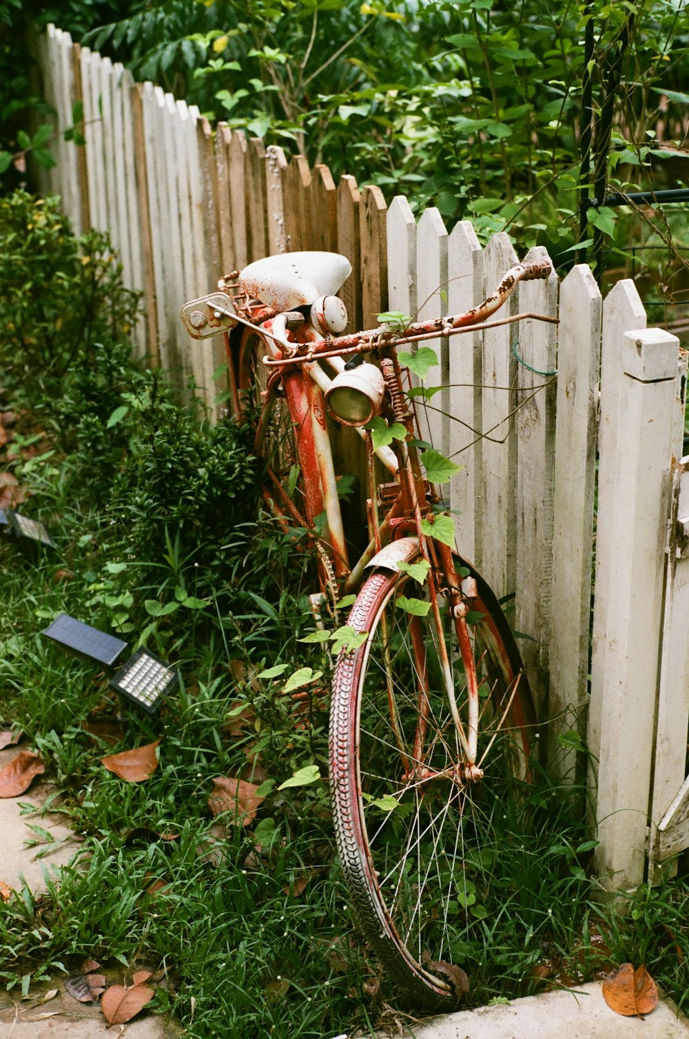 Ein altes rostiges Fahrrad, das an einem weißen Lattenzaun lehnt