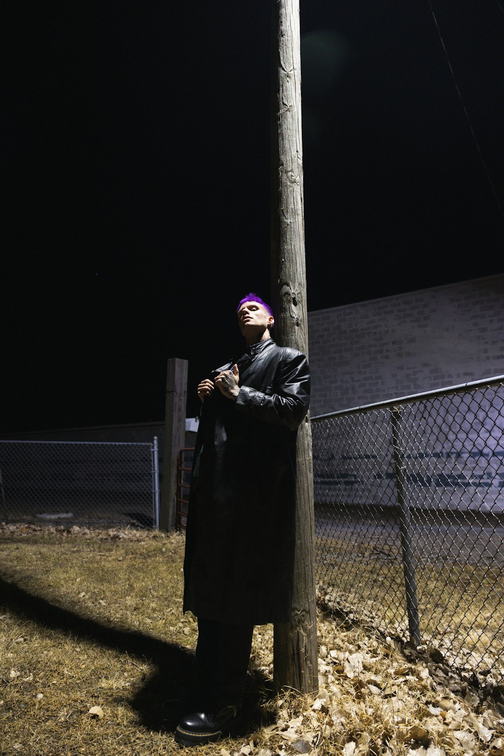 a man leaning against a telephone pole at night
