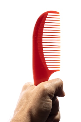 A hand holding a bright red plastic comb with a curved handle, set against a plain white background.