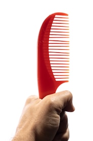 A hand holding a bright red plastic comb with a curved handle, set against a plain white background.