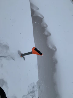 An instructor demonstrating avalanche rescue techniques with a beacon and probe in a snowy field.