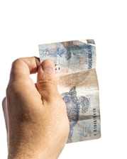 A hand holding a slightly worn two reais banknote with a turtle illustration, against a plain white background.