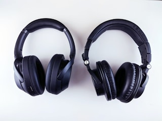 A pair of black over-ear headphones is placed against a white background. The headphones have thick, padded ear cups and an adjustable headband, with one labeled 'L' and the other 'R' for left and right sides.