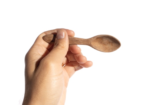 A close-up of a handcrafted wooden spoon resting on a rustic cutting board surrounded by fresh herbs.