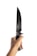A hand is gripping a large knife with intricate, ornamental metalwork on the handle against a plain white background. The knife has a long, sharp blade.