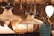 A collection of vintage pendant lamps and light fixtures hang from the ceiling in a dimly lit room, showcasing a variety of glass and metal designs. The lamps have intricate details with some featuring ribbed glass and metal chains. Tags dangle from each lamp, possibly for sale or identification purposes. The warm glow of the bulbs creates a cozy and inviting atmosphere.