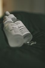 A close-up of a sleek Lavista Tag skincare bottle resting on soft white fabric with gentle natural light.