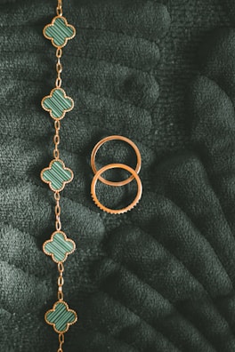 A flat lay of 18k gold bracelets arranged on a cream surface with a hint of garden greenery.