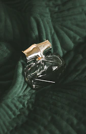A bronze and yellow accented perfume bottle on a textured fabric, evoking warmth and sophistication.
