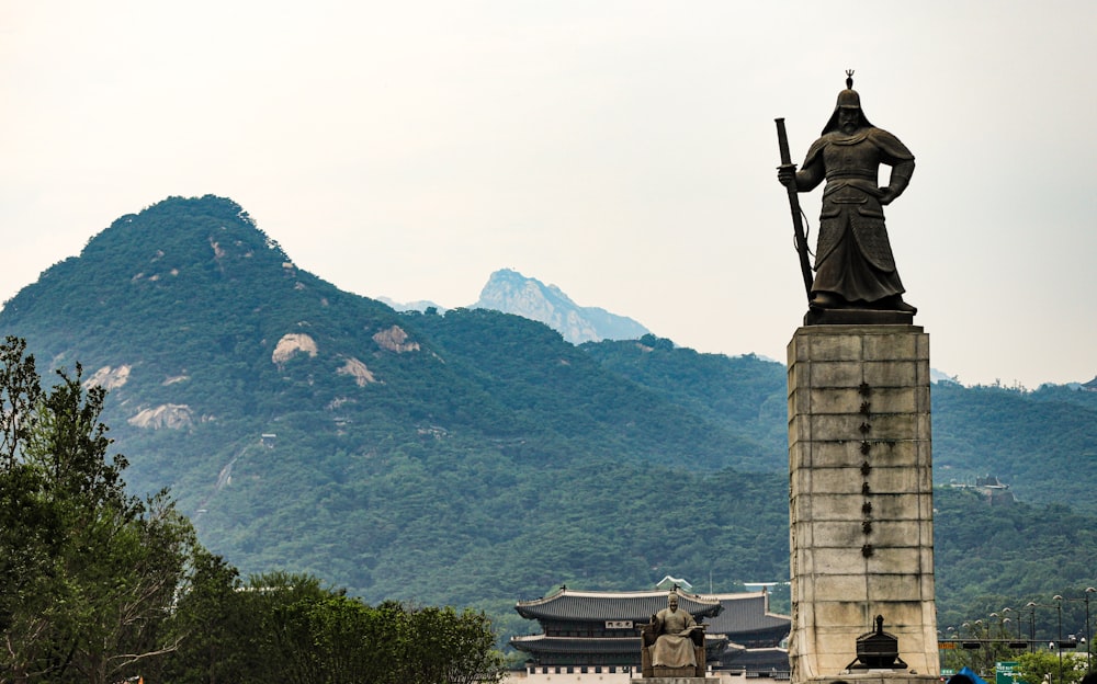 a statue of a woman holding a staff in front of a mountain