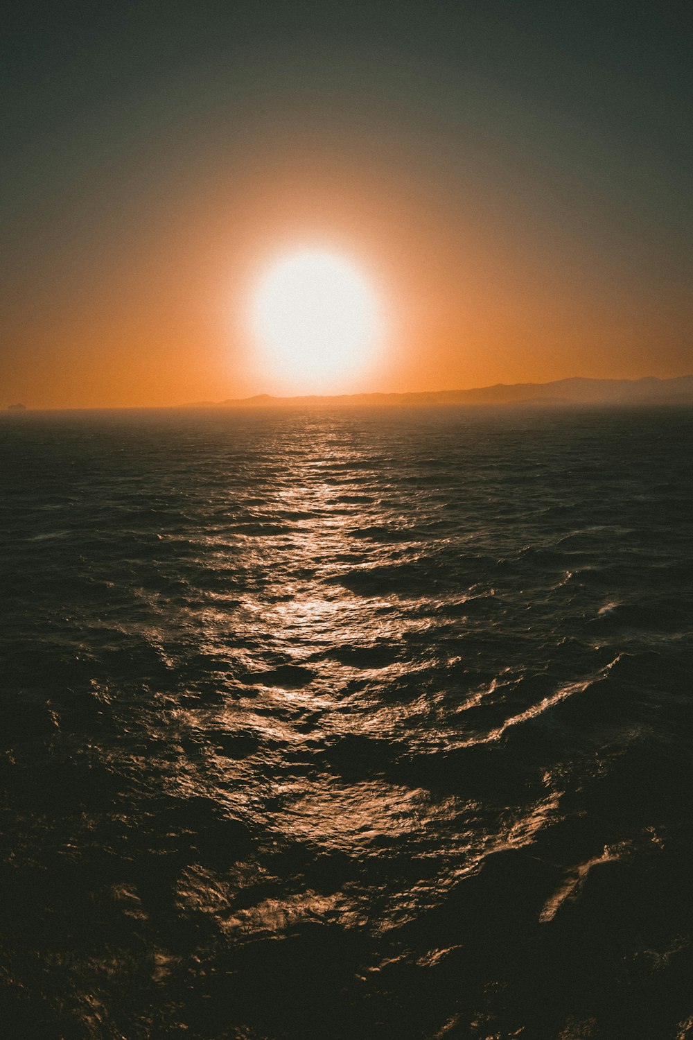 a large body of water with a sun in the background