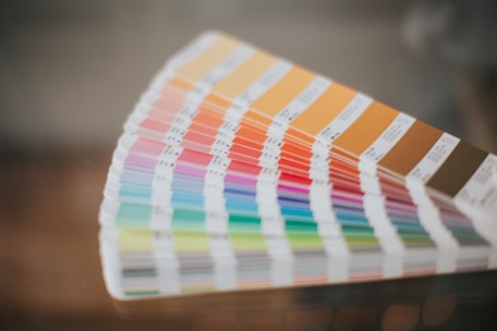 A fan of color swatches arranged in a gradient pattern, displaying a wide range of hues from warm oranges and browns to cool blues and greens. The swatches are shown in a curved formation, with labels indicating different shades.