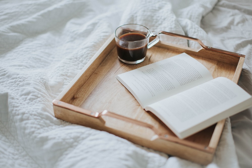 a cup of coffee and an open book on a tray