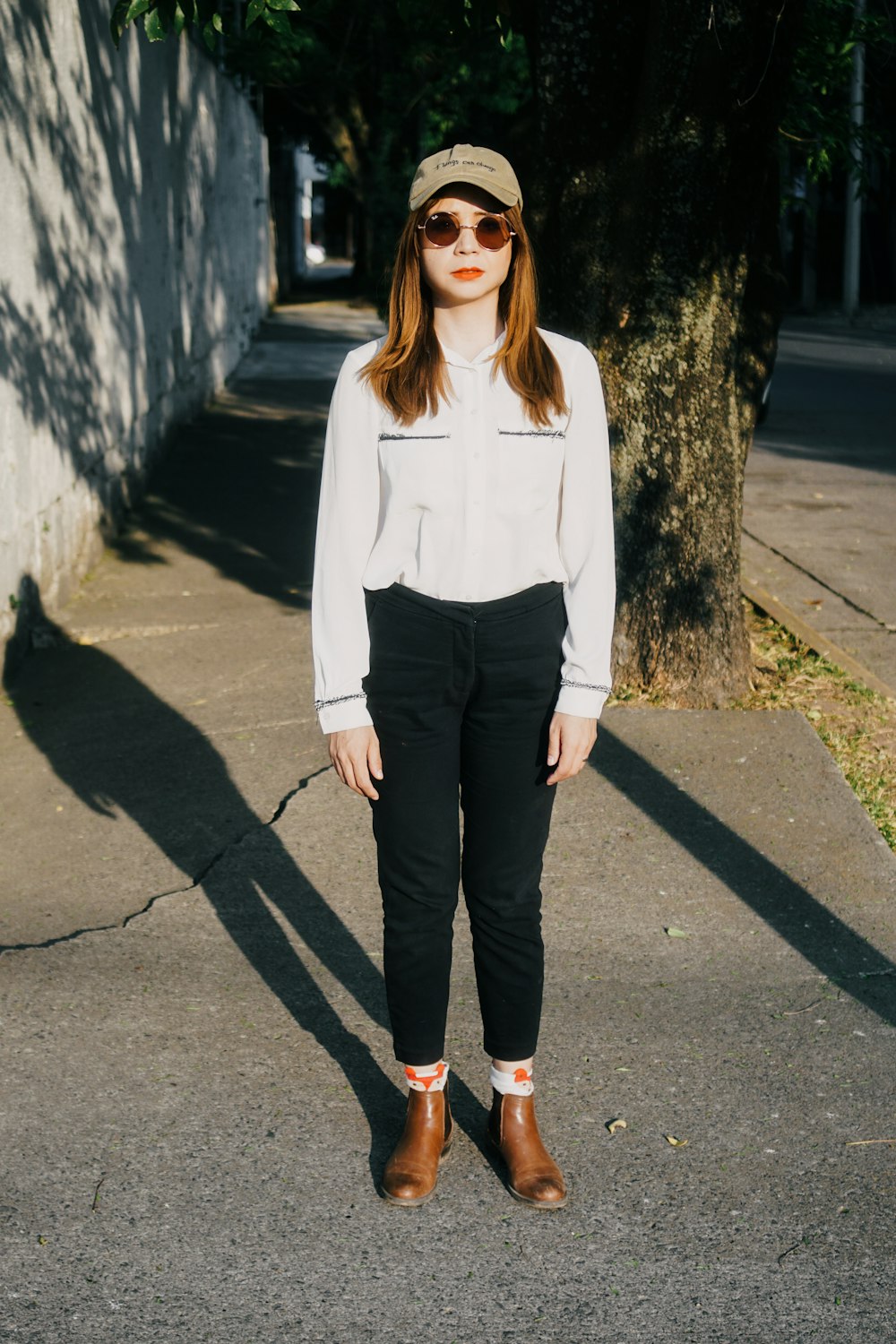 a woman standing on a sidewalk wearing a hat and sunglasses