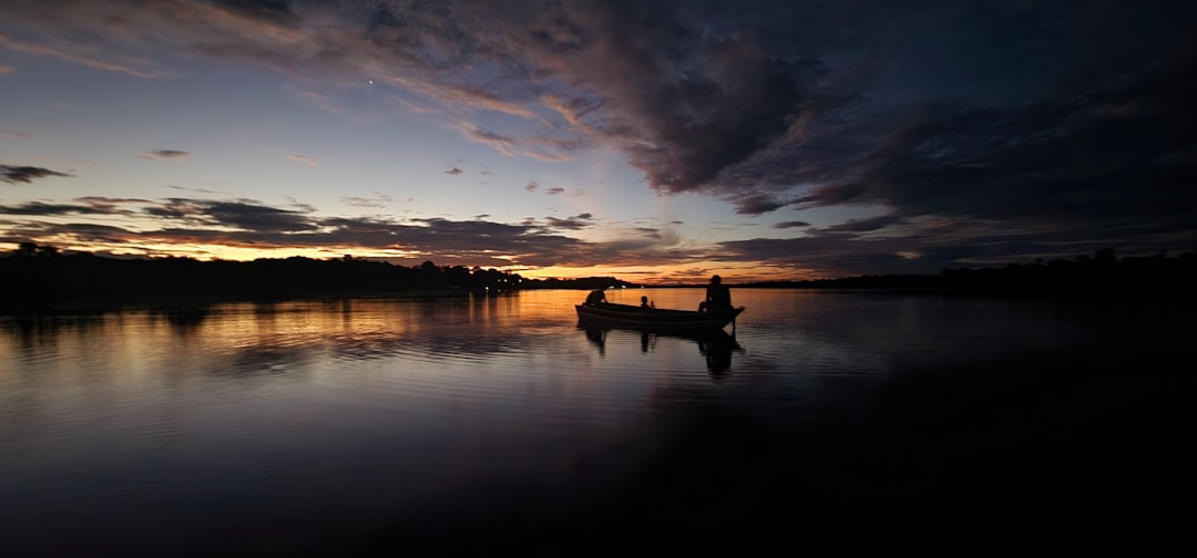 a boat floating on top of a lake under a cloudy sky,