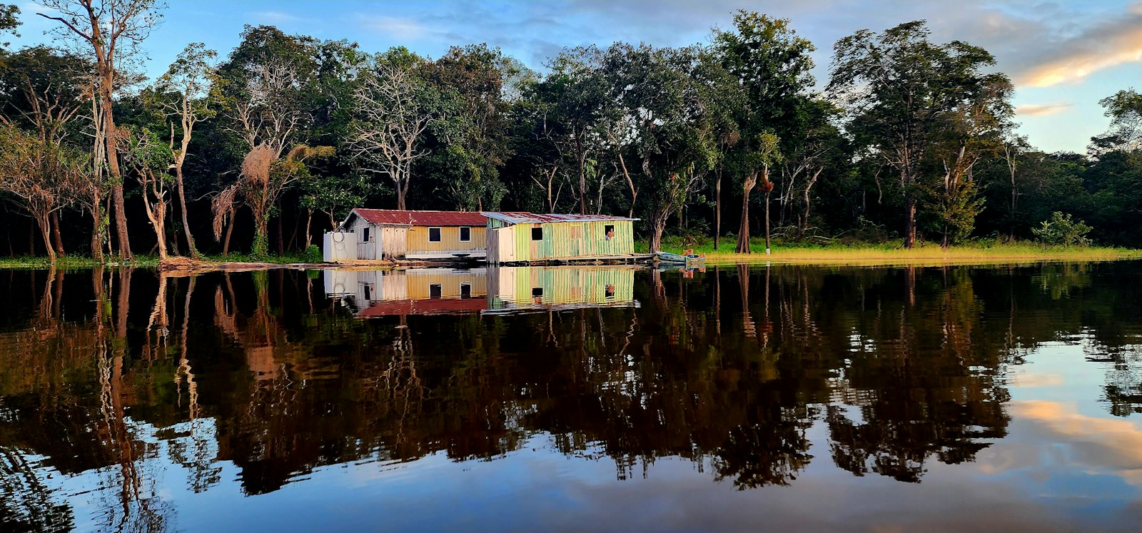 A floating riverside house and rainforest trees mirrored in still Amazon floodwaters near Manaus
