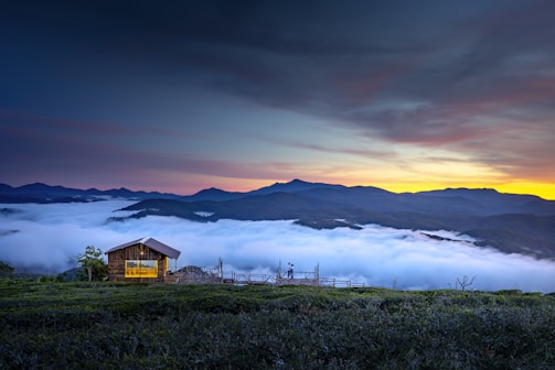 An aerial shot of a cabin perched on a rocky hillside overlooking a misty valley.